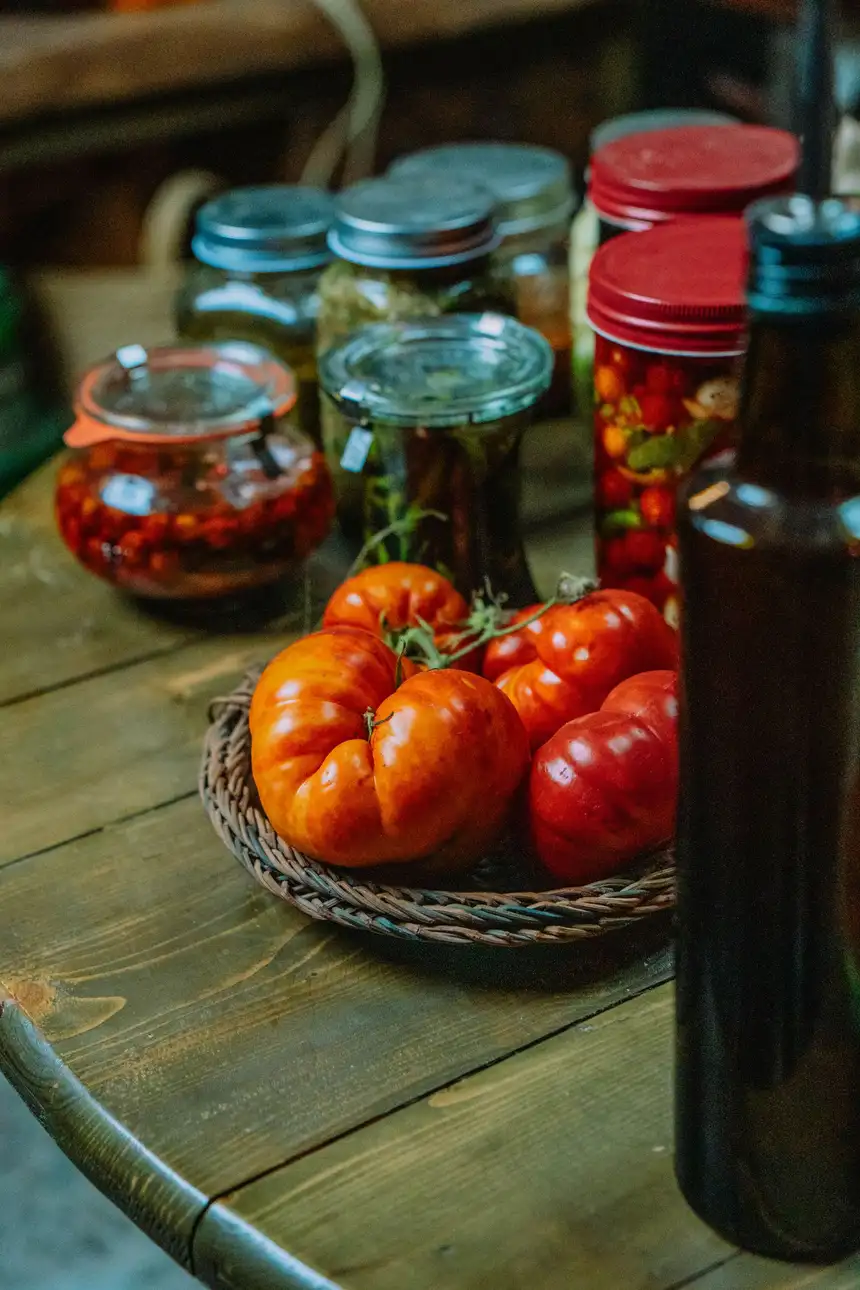 Rustic homemade preserve jars and a bottle of oil arranged on a weathered wooden table.