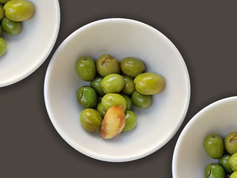 A white bowl of plump green olives on a dark surface.