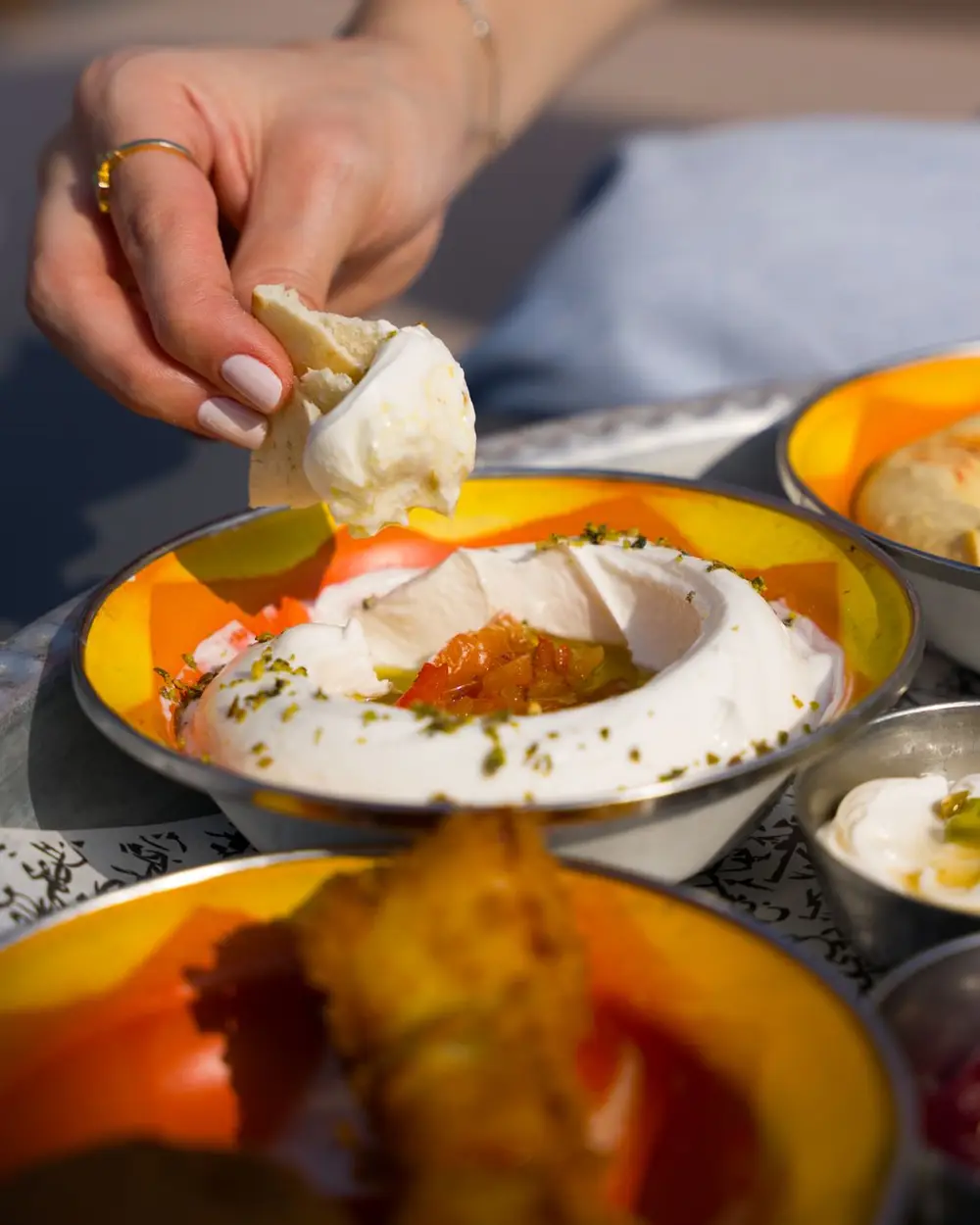 A bowl of soft white labneh drizzled with olive oil, served with bread and pickles.