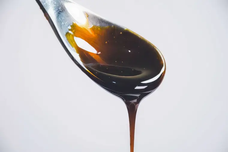 Dark, glossy pomegranate molasses dripping from a spoon against a pale background.