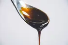 Dark, glossy pomegranate molasses dripping from a spoon against a pale background.